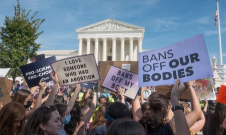 Nebraska abortion bans: Crowd of adults at rally with handmad signs held up gathered in front of multi-story, white building with 8 pillars in front