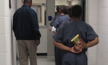 study says schooling for incarcerated youth is inferior: boy in juvenile detention holds book behind back as he walks in line with other detainees