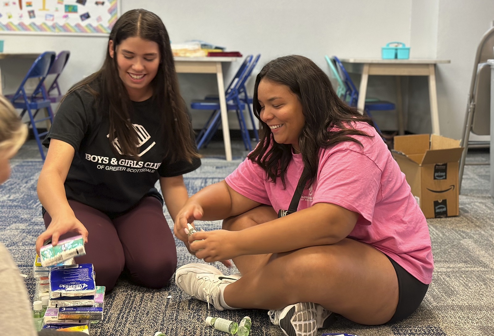 Summer camps are booming: two young women workers on floor smiling while stacking things