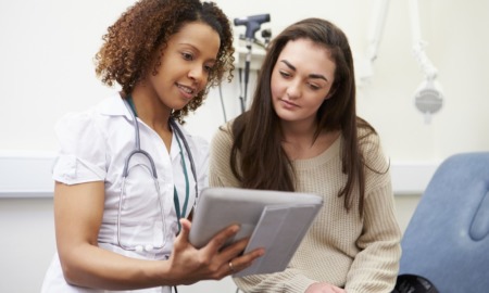 teen interest in long lasting birth control soars: doctor showing teen girl information on tablet device in doctor's office