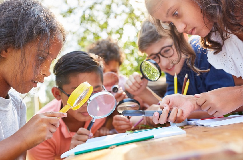 Condition of education report 2024: group of young students outdoors looking at something with magnifying glasses