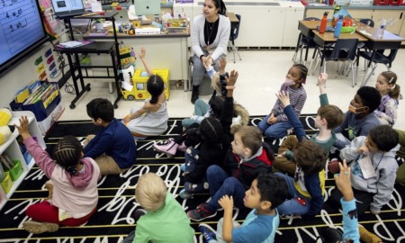 US teacher shortage, HBCU helping to change that: young female teacher of color teaching classroom of children with hands raised