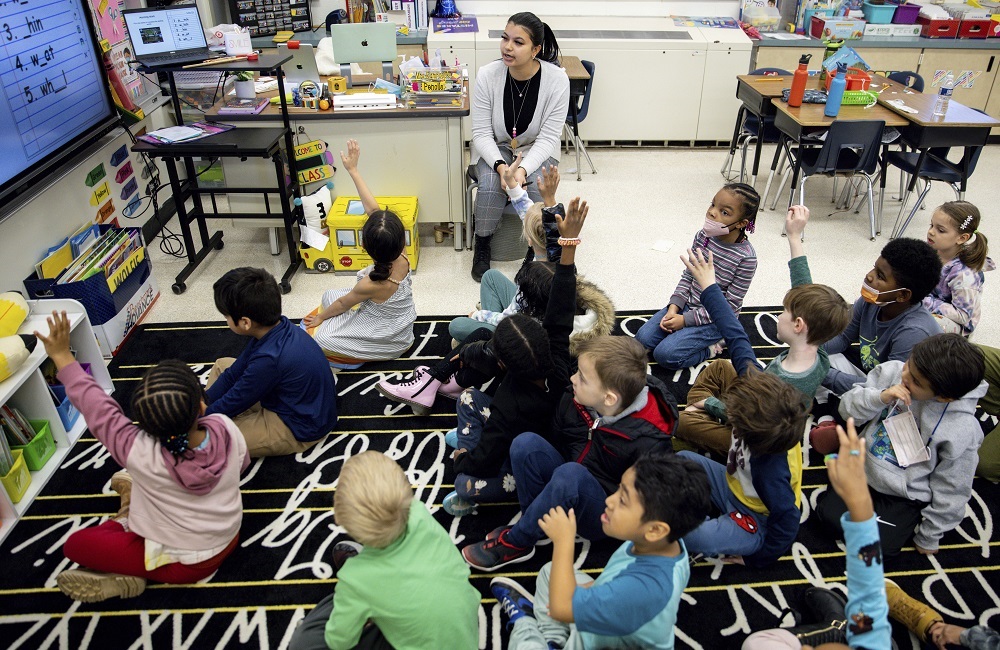 US teacher shortage, HBCU helping to change that: young female teacher of color teaching classroom of children with hands raised