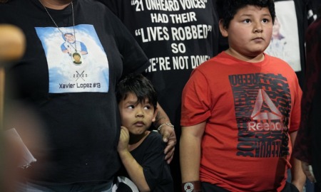 Uvalde families press urgency after California shootings: young boy hugging mother from the side while standing in group next to older boy