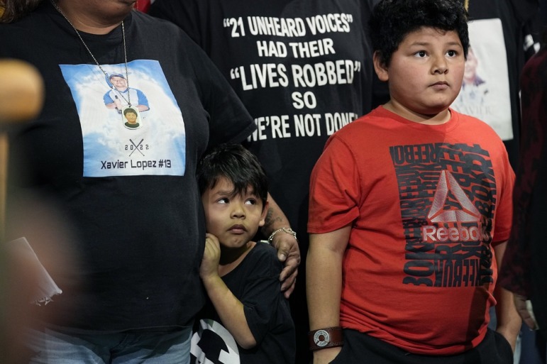 Uvalde families press urgency after California shootings: young boy hugging mother from the side while standing in group next to older boy