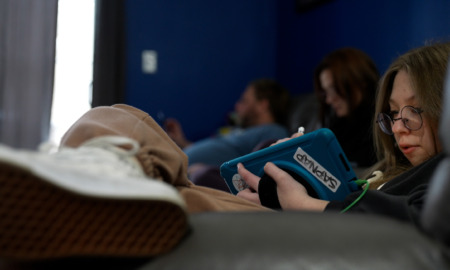 Long COVID in kids-a person with long hair sits with legs crossed using a tablet