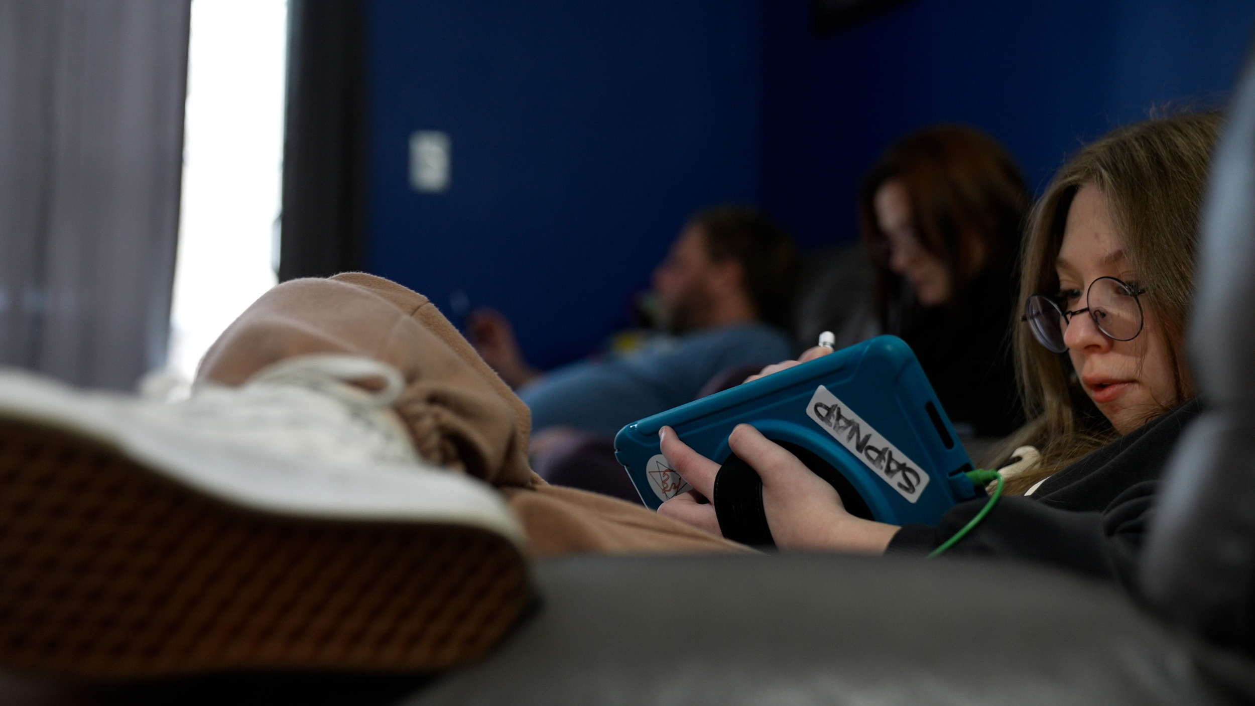 Long COVID in kids-a person with long hair sits with legs crossed using a tablet