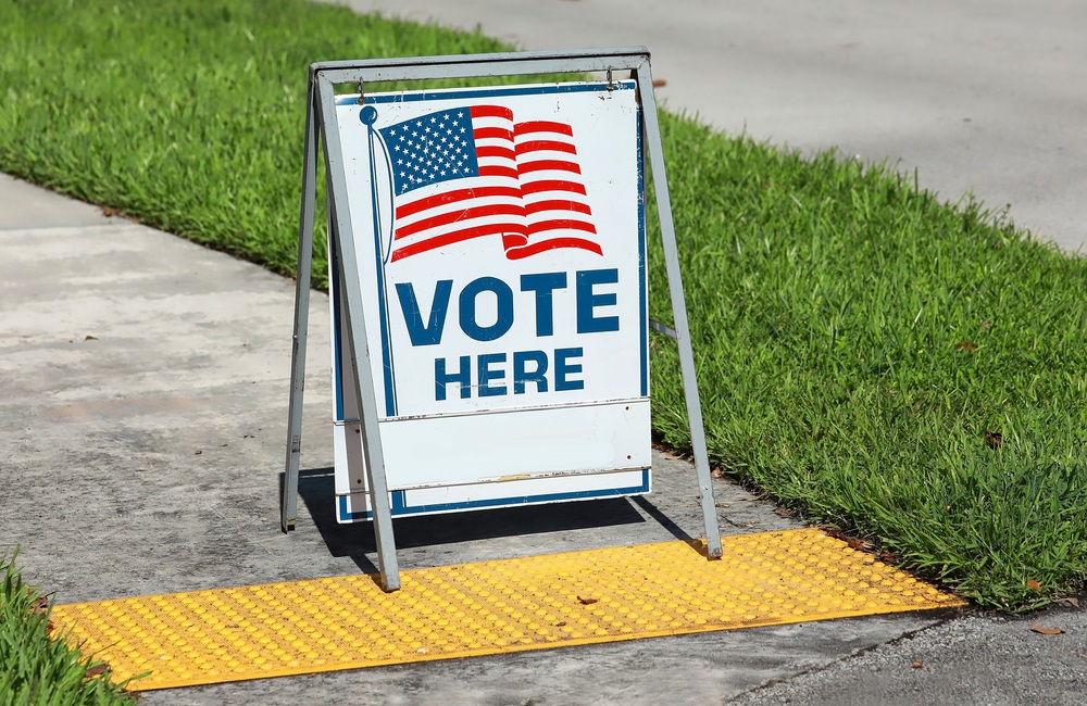 voting sign on sidewalk: "Vote Here" and American flag graphic on folding sidewalk sign