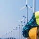 green jobs: woman engineer in reflective vest holding hard hat and looking at wind turbines