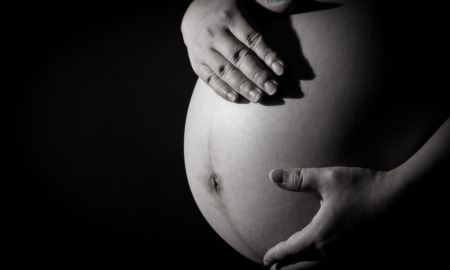 Debate over U.S. maternal mortality rates: pregnant belly with hands caressing against black background