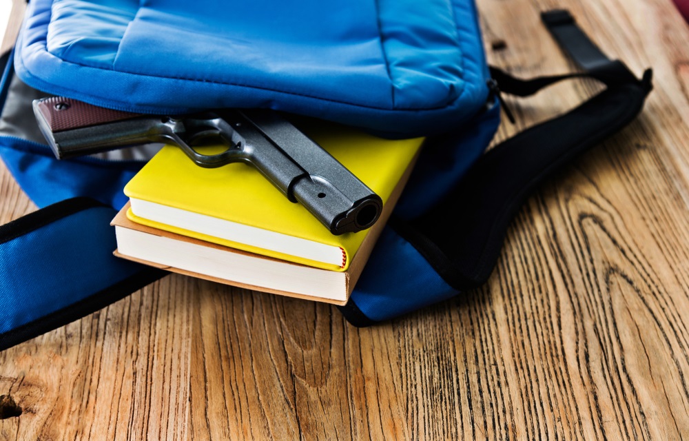 student threats, when students bring guns to schools: gun falling out of backpack on top of yellow book