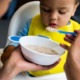 Supplemental nutrition, WIC, food access: baby with yellow bib being fed porridge